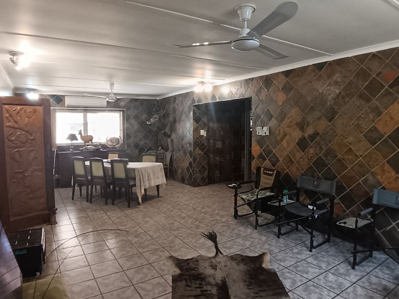 Spacious open-plan living and dining area featuring stone wall cladding, tiled flooring, and ceiling fans, offering a versatile layout for family living.