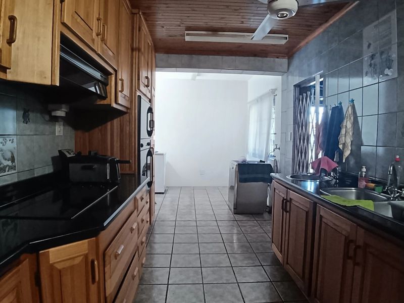 A functional kitchen featuring wooden cabinetry, black granite countertops, built-in oven, hob, and a double stainless steel sink with tiled flooring and a wooden ceiling.
