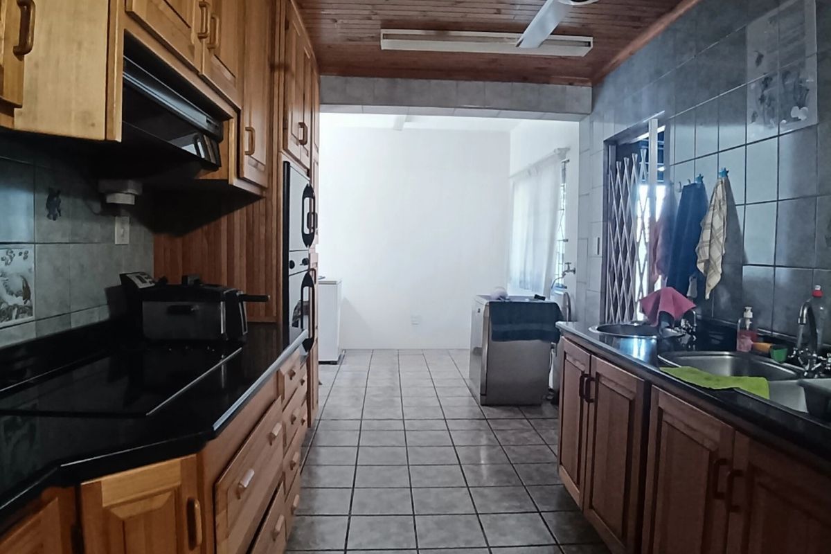 A functional kitchen featuring wooden cabinetry, black granite countertops, built-in oven, hob, and a double stainless steel sink with tiled flooring and a wooden ceiling.