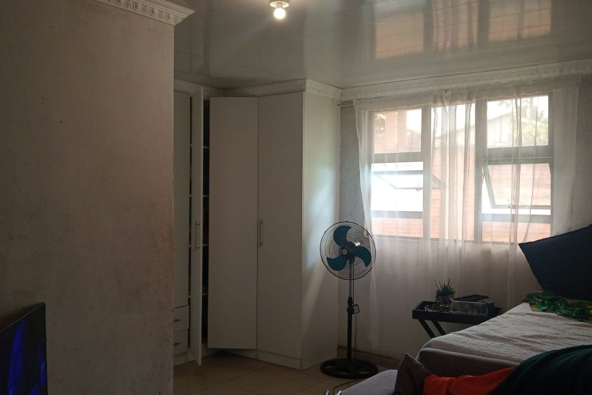A bedroom featuring built-in cupboards, tiled flooring, and decorative ceiling cornicing. The room requires cosmetic updates to the wall finishes.