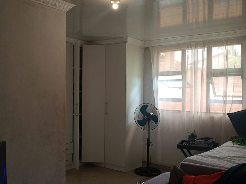 A bedroom featuring built-in cupboards, tiled flooring, and decorative ceiling cornicing. The room requires cosmetic updates to the wall finishes.