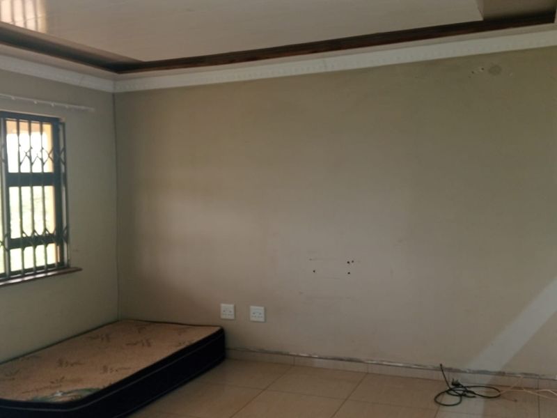 Open plan living area featuring tiled floors, security bars on windows, and basic kitchen cabinetry. The space requires minor cosmetic repairs and wall maintenance.