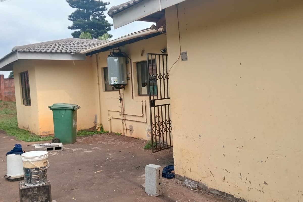 Rear exterior view of the property showing a concrete patio area, external geyser, and security gate access.