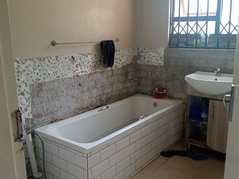 A bathroom requiring renovation, featuring a bathtub with tiled surround, a vanity basin, and significant wall finish damage.