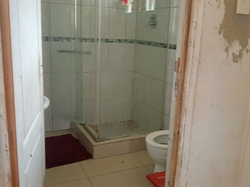 A bathroom featuring a glass shower enclosure, toilet, and pedestal basin, currently requiring significant wall repairs and cosmetic updates to improve its condition.