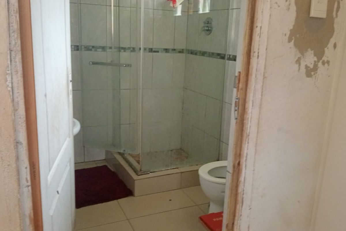 A bathroom featuring a glass shower enclosure, toilet, and pedestal basin, currently requiring significant wall repairs and cosmetic updates to improve its condition.