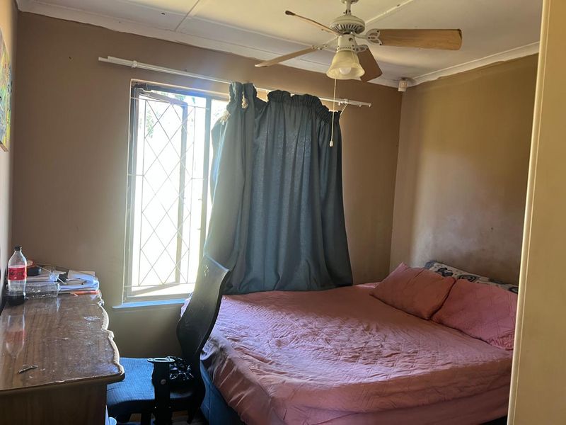 A bedroom featuring a ceiling fan and a window with security bars, requiring cosmetic updates to the wall finishes.