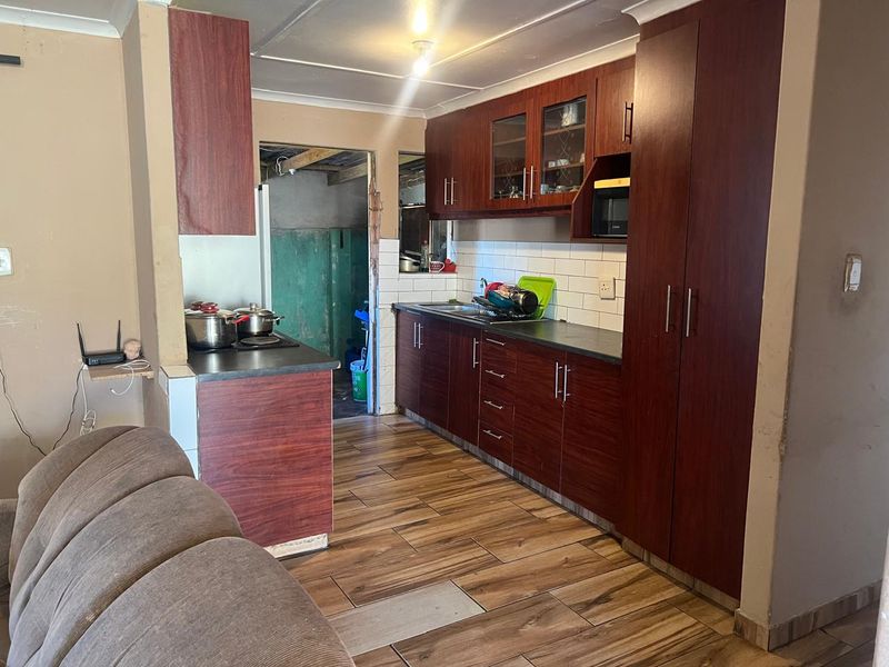 A functional kitchen featuring dark wood-finish cabinetry, subway tile backsplash, and wood-look floor tiles, requiring some finishing work to improve overall presentation.