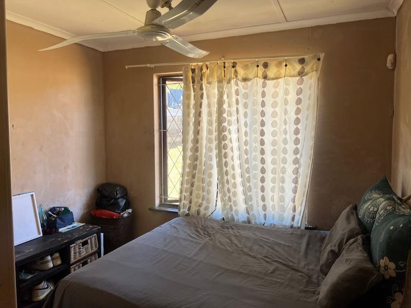 A bedroom featuring a ceiling fan and a window with security bars, requiring cosmetic updates to the wall finishes.