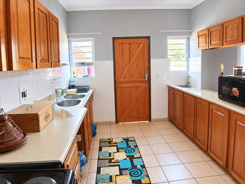 A functional kitchen featuring wooden cabinetry, dual sink areas, tiled splashbacks, and ceramic flooring, offering a practical layout with natural light from louvre windows.