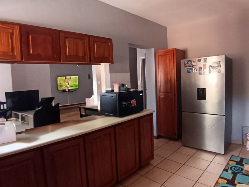Open plan kitchen area featuring wooden cabinetry, tiled flooring, and a breakfast counter, flowing into the adjacent living space.