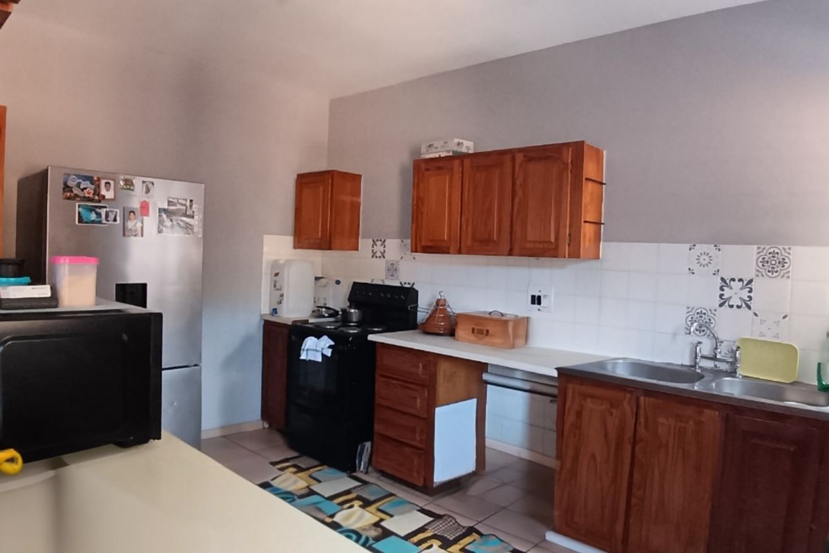 A functional kitchen featuring wooden cabinetry, laminate countertops, a double basin sink, and a tiled backsplash, offering potential for modern updates.