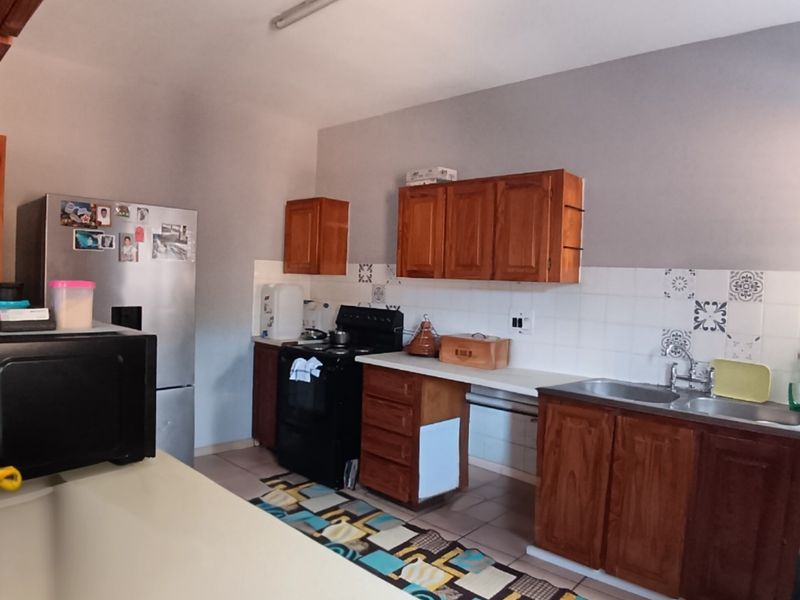 A functional kitchen featuring wooden cabinetry, laminate countertops, a double basin sink, and a tiled backsplash, offering potential for modern updates.