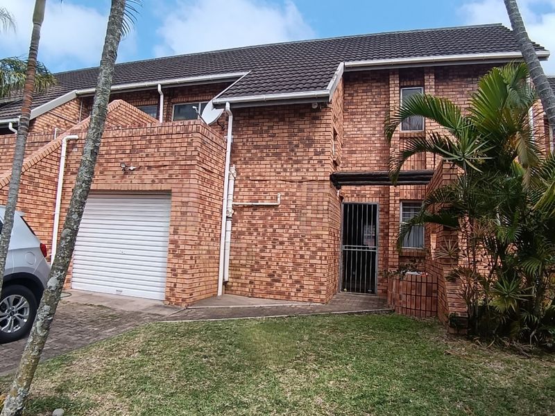 Front elevation of a face brick townhouse featuring a single garage, paved driveway, and secure entrance gate.