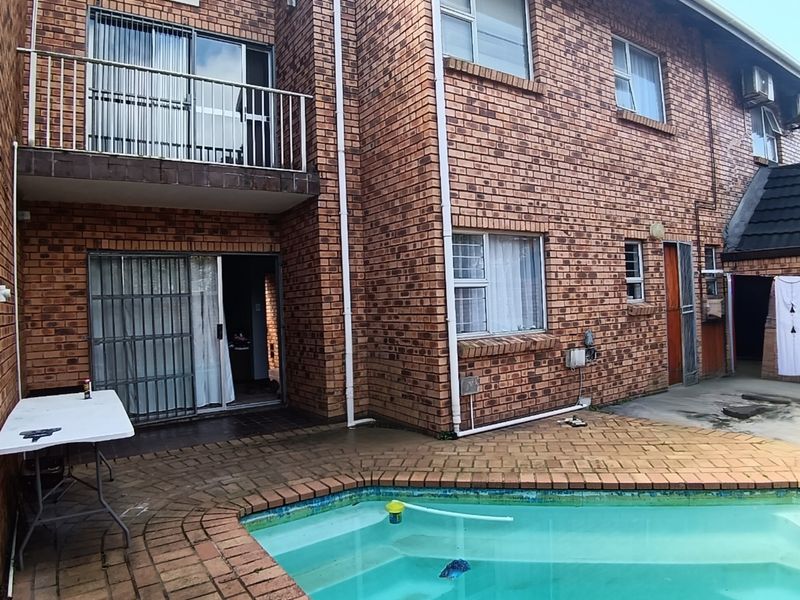 Rear exterior view of a townhouse featuring a brick facade, a private swimming pool, a paved patio area, and an upper-level balcony.