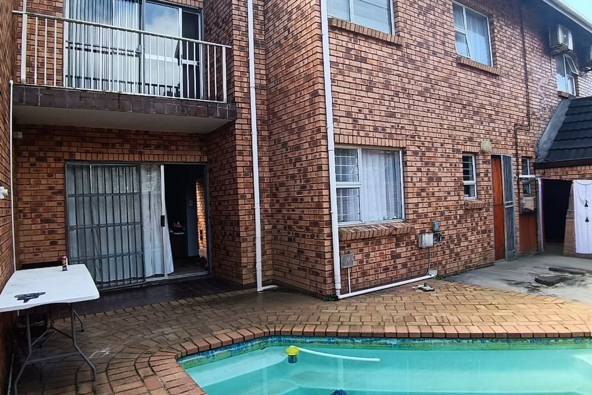 Rear exterior view of a townhouse featuring a brick facade, a private swimming pool, a paved patio area, and an upper-level balcony.