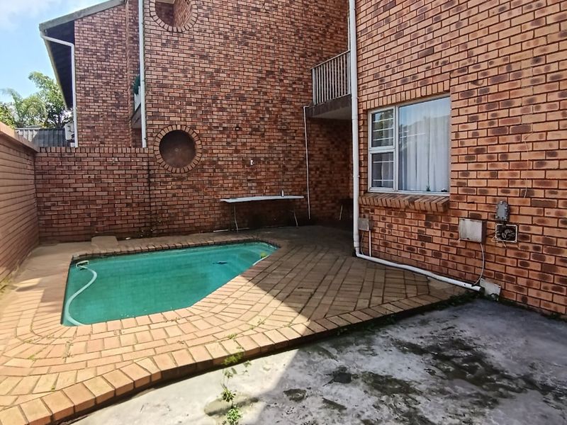 Rear courtyard area featuring a small swimming pool, brick paving, and a face brick townhouse facade with a balcony.
