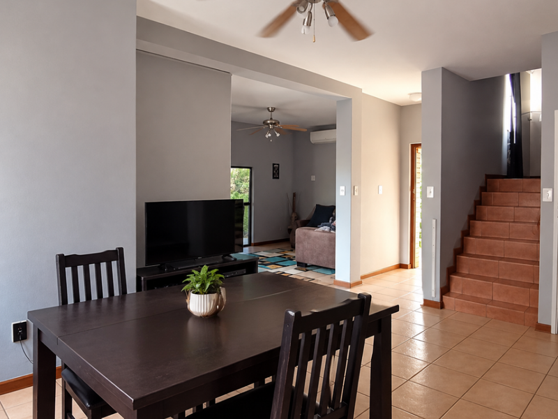 Open plan living and dining area featuring tiled flooring, a ceiling fan, and a staircase leading to the upper level.