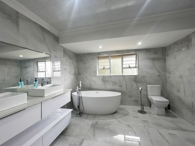Modern, well-appointed bathroom featuring a sleek freestanding bathtub, double vanity with contemporary basins, and floor-to-ceiling marble-look tiling.
