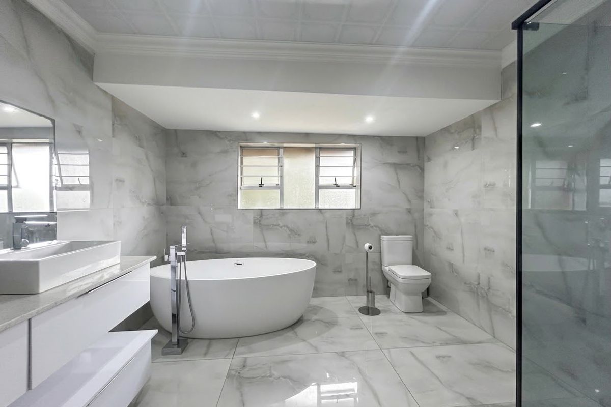 Modern, high-end bathroom featuring floor-to-ceiling marble-look tiles, a sleek freestanding bathtub, a wall-mounted vanity with a vessel sink, and a glass-enclosed shower.