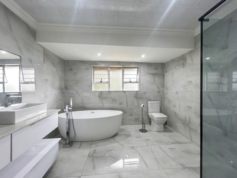 Modern, high-end bathroom featuring floor-to-ceiling marble-look tiles, a sleek freestanding bathtub, a wall-mounted vanity with a vessel sink, and a glass-enclosed shower.