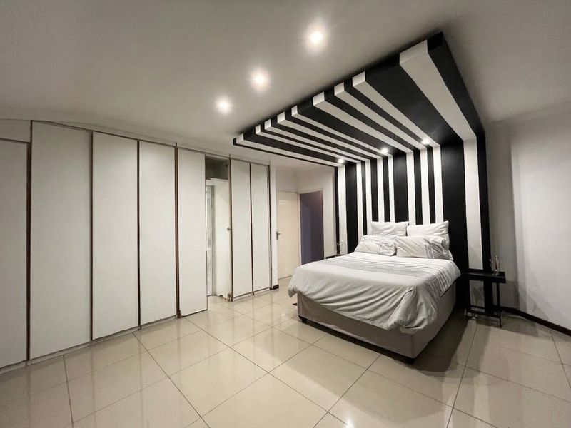 Spacious bedroom featuring large built-in cupboards, polished tile flooring, and a striking black and white decorative ceiling and wall feature.