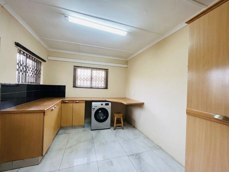 A functional laundry room featuring built-in wooden cabinetry, laminate countertops, tiled flooring, and security bars on the windows.