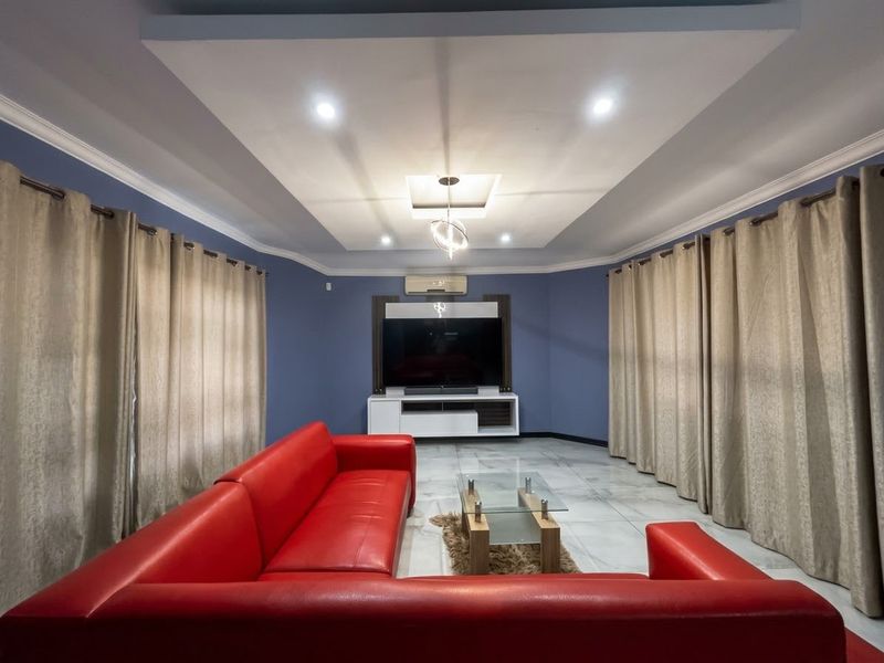 A well-maintained living room featuring a recessed ceiling with cove lighting, tiled floors, and a split-system air conditioner.