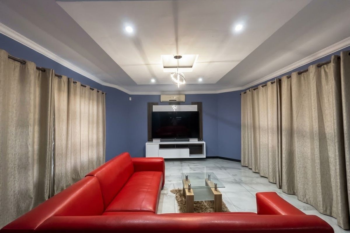 A well-maintained living room featuring a recessed ceiling with cove lighting, tiled floors, and a split-system air conditioner.