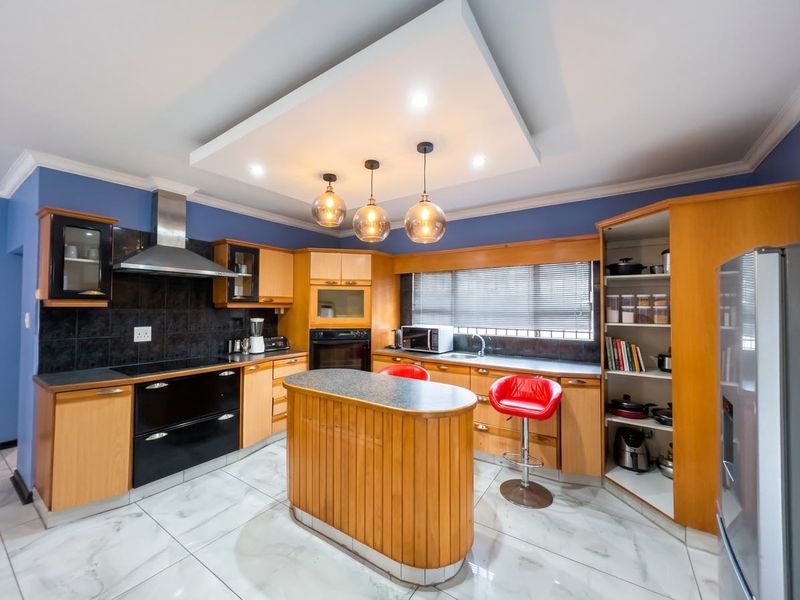 A well-appointed kitchen featuring wooden cabinetry, a central island, built-in appliances, and modern tiled flooring under a stylish drop ceiling.