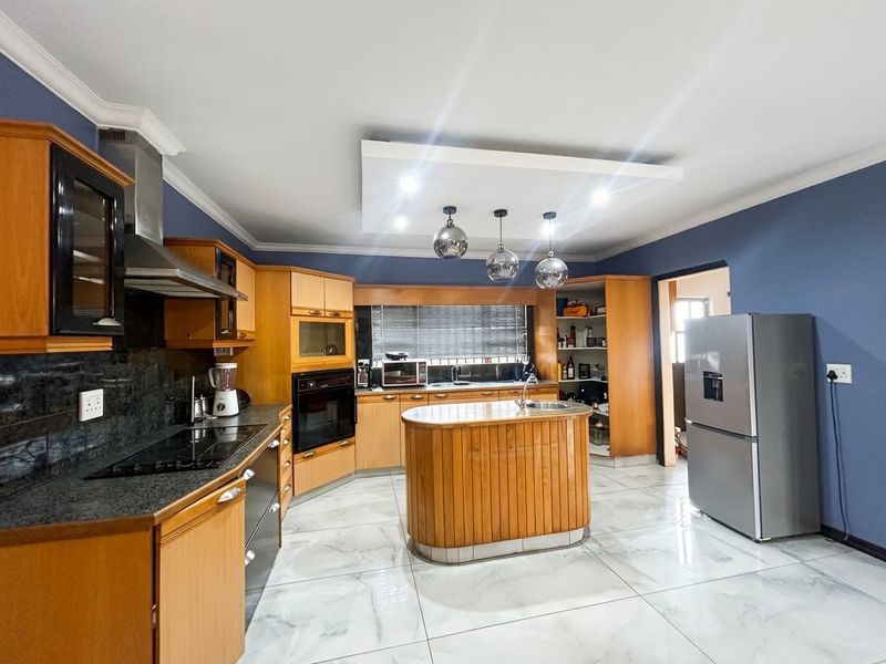 Spacious kitchen featuring warm wooden cabinetry, granite countertops, a central island with a prep sink, and modern tiled flooring.