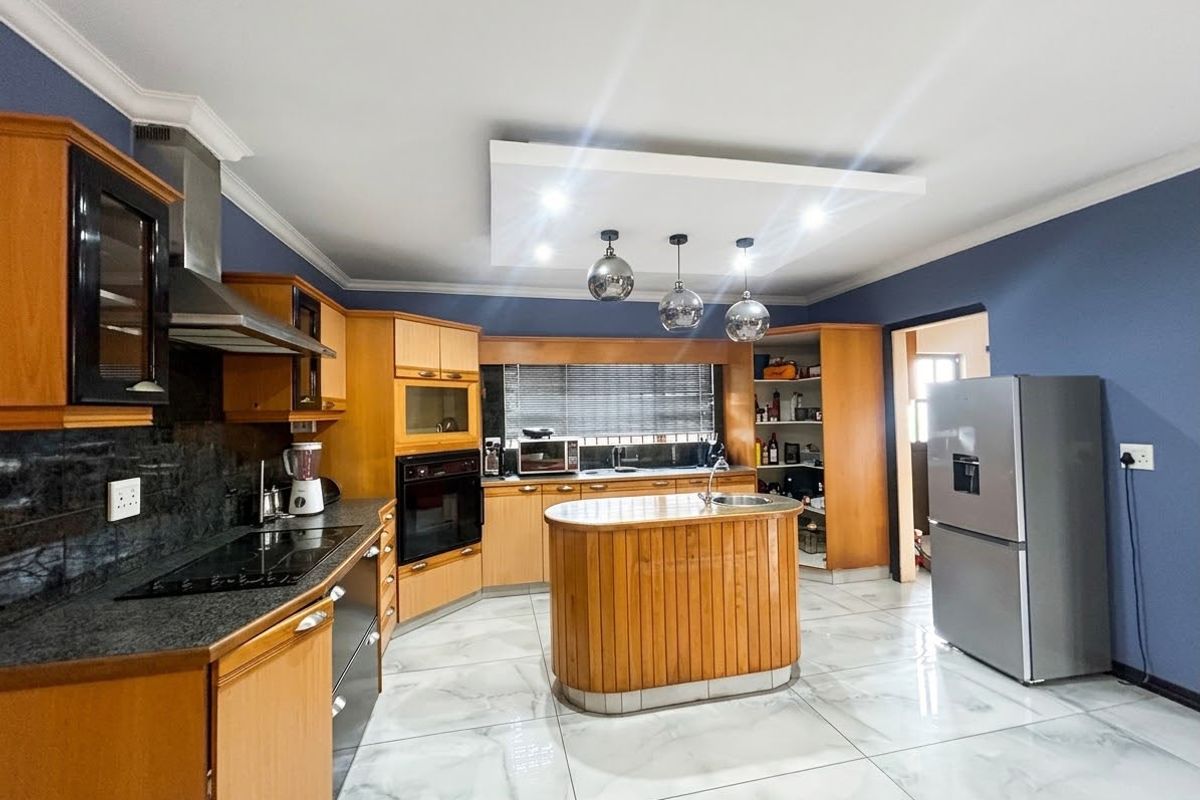 Spacious kitchen featuring warm wooden cabinetry, granite countertops, a central island with a prep sink, and modern tiled flooring.