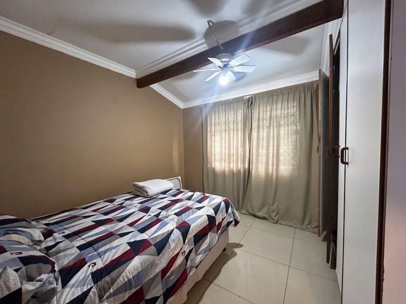 A bedroom featuring tiled flooring, a ceiling fan, an exposed timber beam, and built-in wardrobe storage.