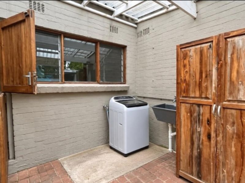 Outdoor laundry area featuring a utility sink, brick walls, and timber cabinetry under a pergola structure.