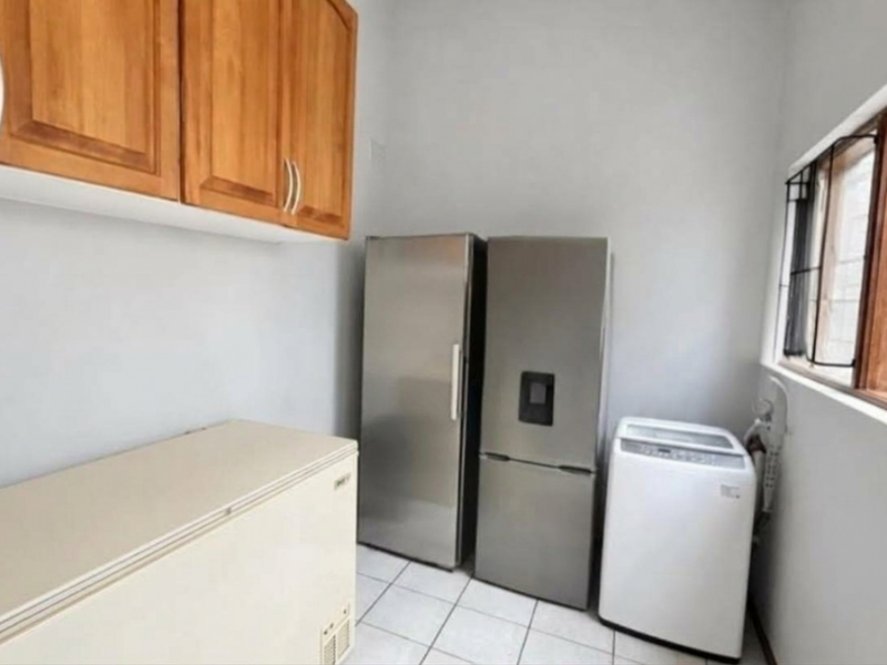 A functional laundry room featuring wooden wall-mounted cabinetry, tiled flooring, and a window with security bars, providing practical utility space.