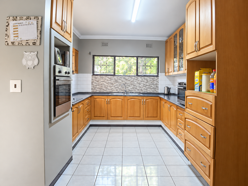 A functional U-shaped kitchen featuring warm-toned wooden cabinetry, tiled flooring, a built-in oven, and a tiled backsplash with ample storage space.