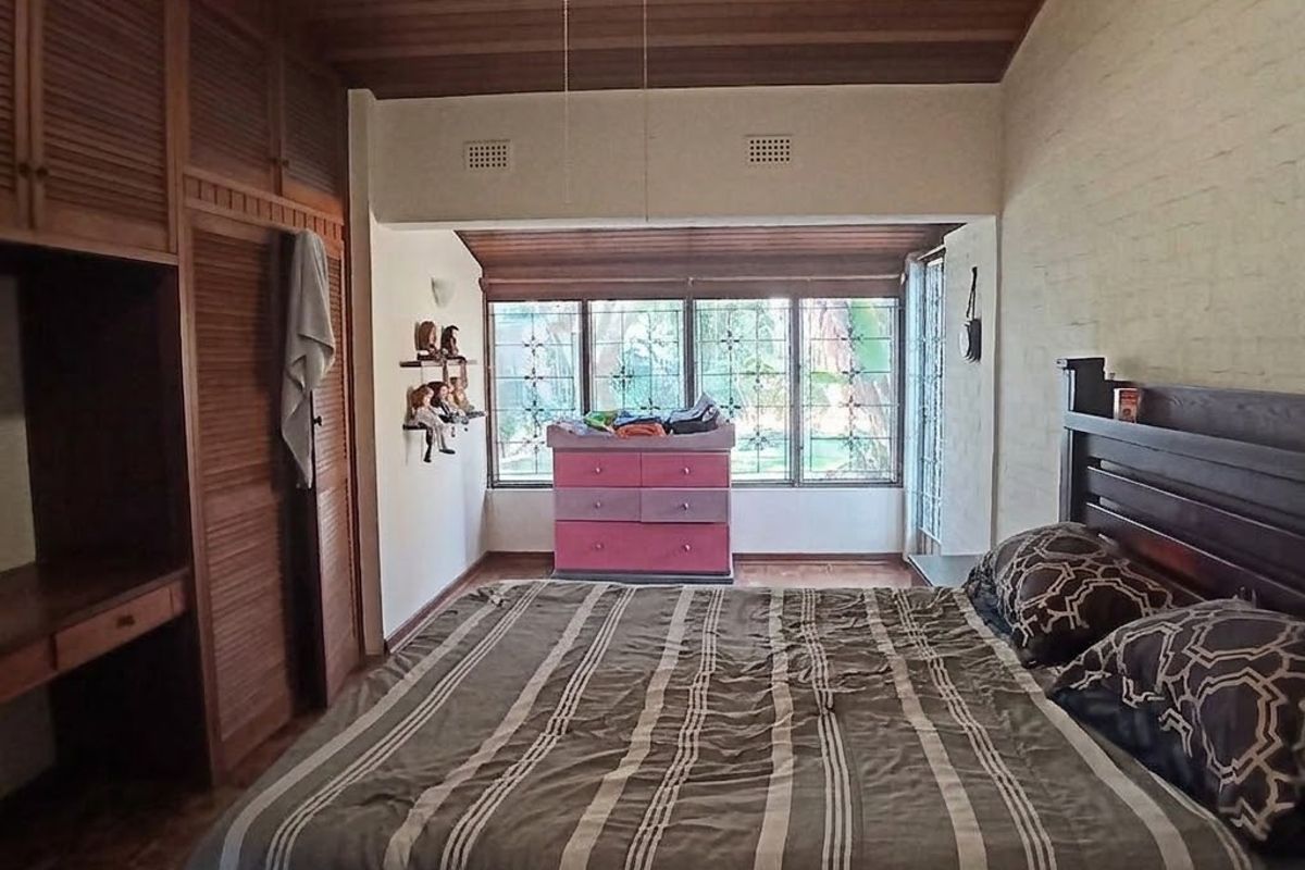 A bedroom featuring built-in wooden cabinetry, a timber-clad ceiling, and large windows with security bars, offering a functional and traditional layout.