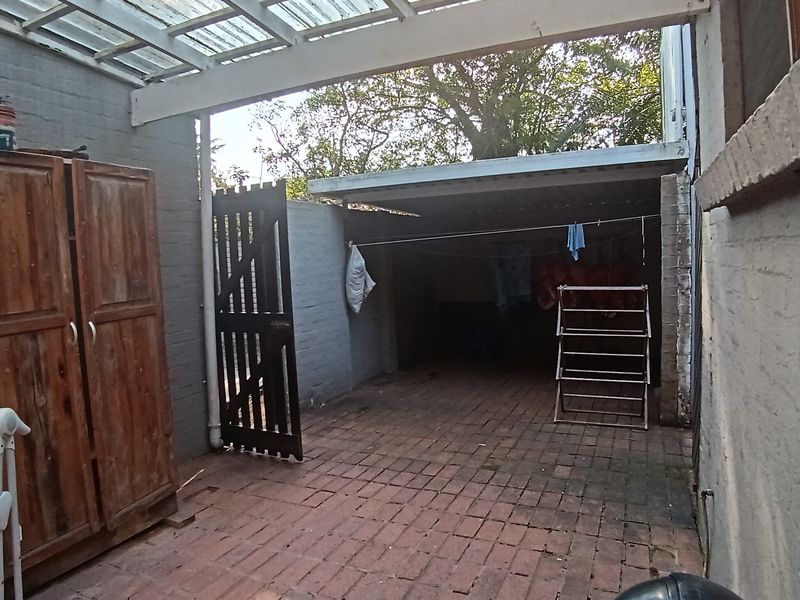 A covered outdoor patio area featuring brick paving, painted brick walls, and a translucent roof structure, suitable for a utility or storage space.