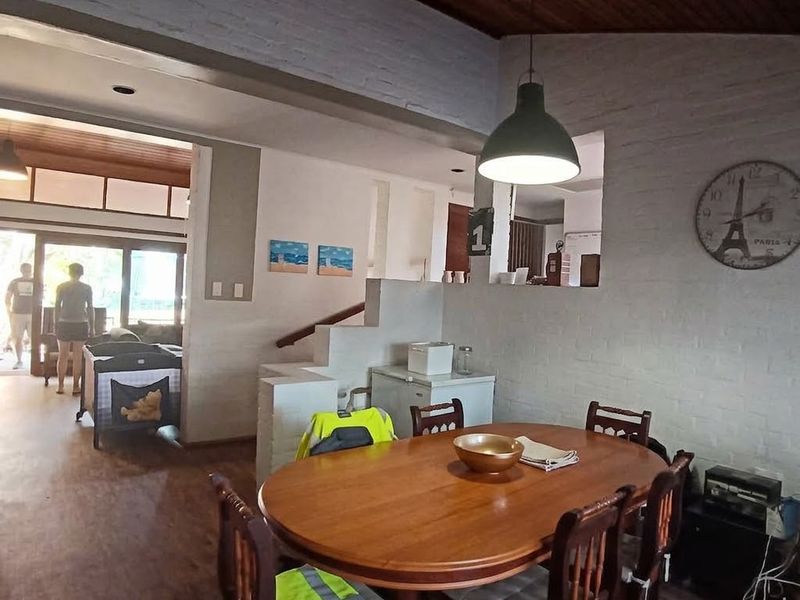 Open plan dining area featuring timber ceilings, painted brick walls, and a pass-through window connecting to the kitchen space.