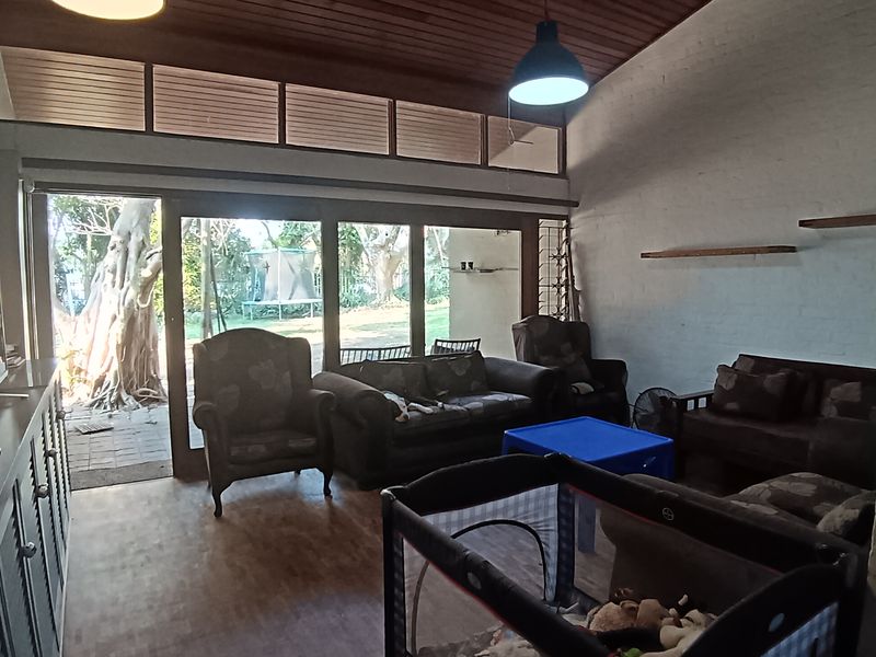 Spacious living room featuring a vaulted timber ceiling, parquet flooring, and large sliding doors that provide abundant natural light and access to the garden.