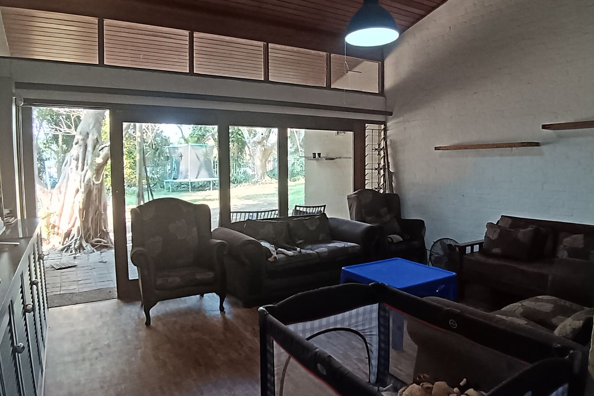Spacious living room featuring a vaulted timber ceiling, parquet flooring, and large sliding doors that provide abundant natural light and access to the garden.