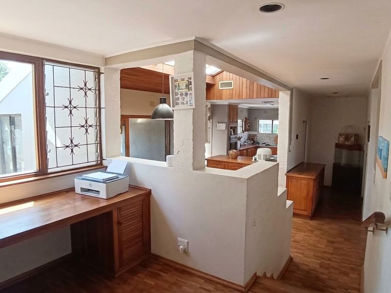 Open plan living area featuring parquet flooring, a built-in timber desk, and a view through to the kitchen area.