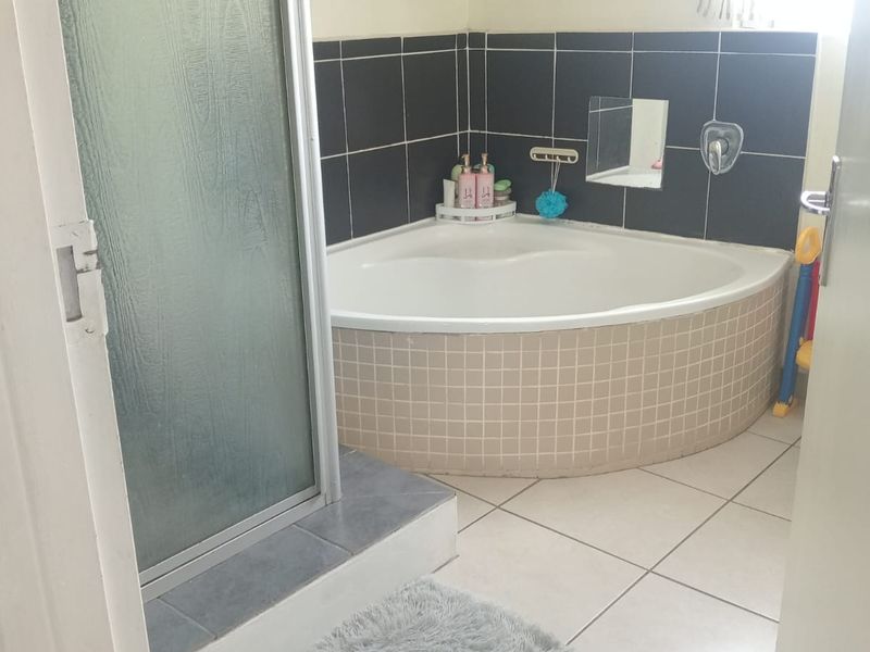 Bathroom featuring a corner bathtub with dark tiled surround, a separate shower enclosure, and neutral ceramic floor tiling.