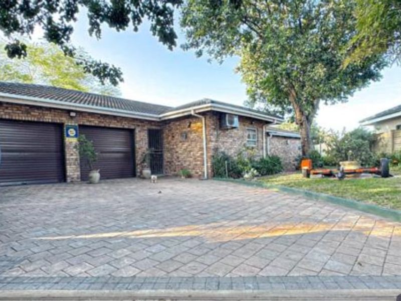 Front exterior view of a brick house featuring a double garage, paved driveway, and established garden area.
