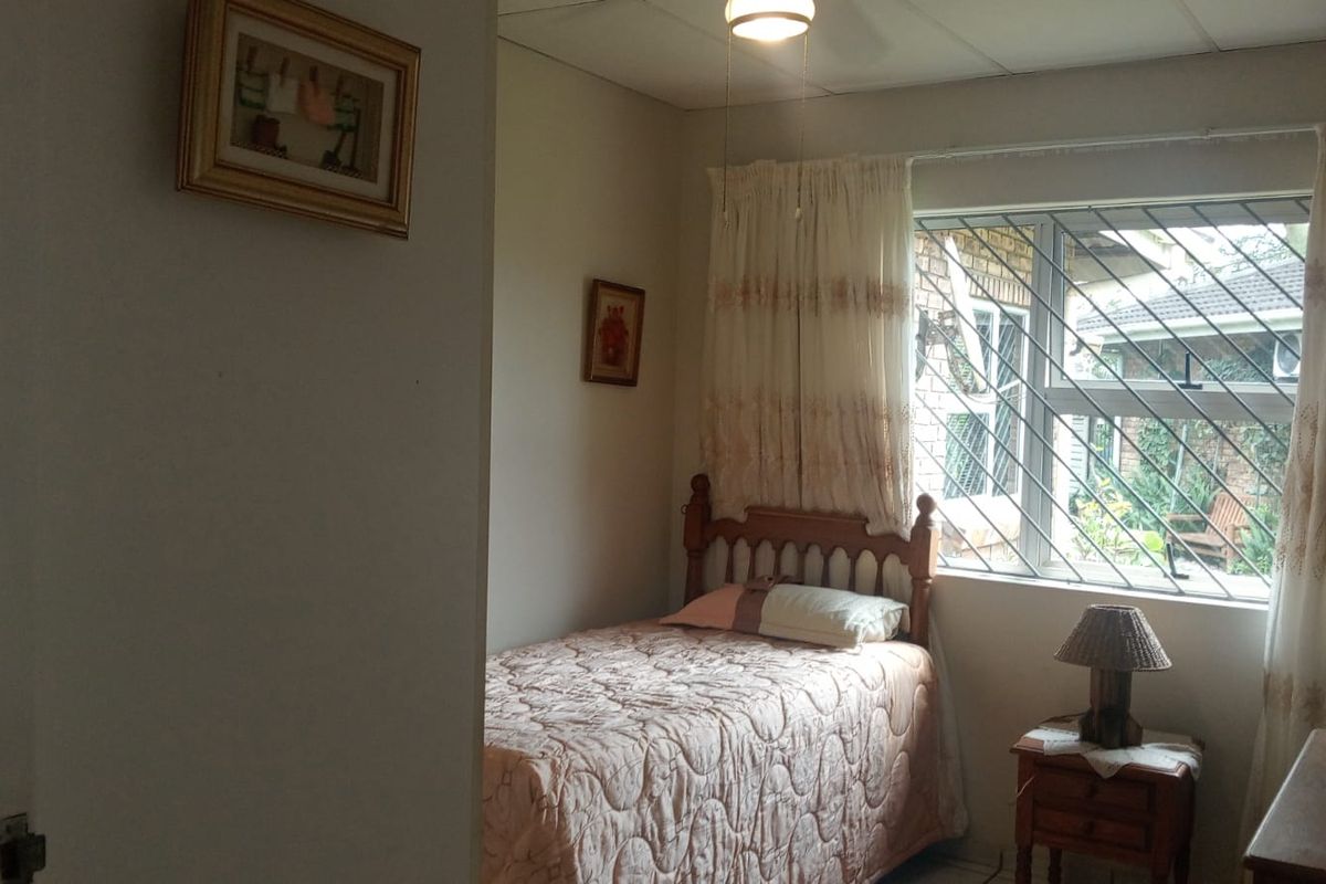 A functional bedroom featuring security bars on the window and a ceiling fan, offering a comfortable and secure living space.