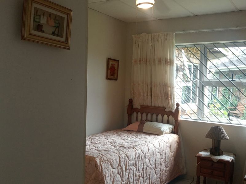 A functional bedroom featuring security bars on the window and a ceiling fan, offering a comfortable and secure living space.