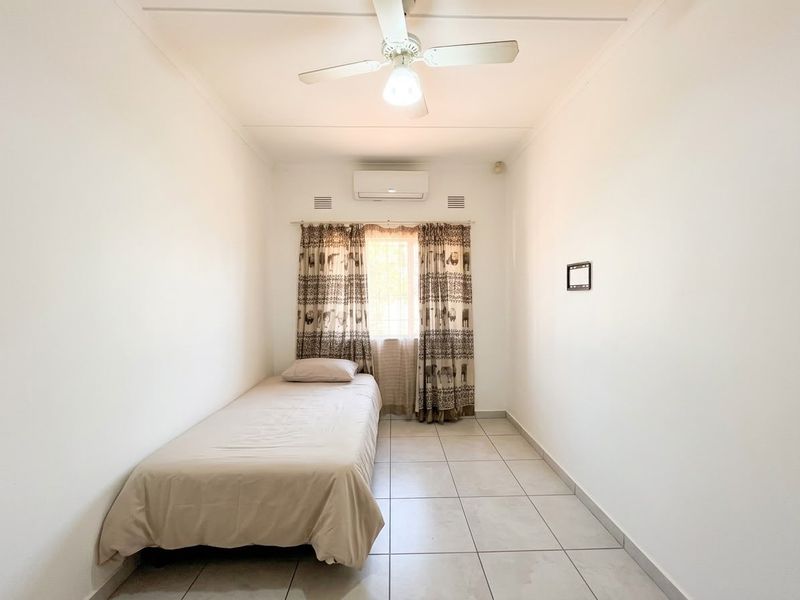 A simple bedroom featuring tiled flooring, a ceiling fan, and a wall-mounted split-system air conditioner.
