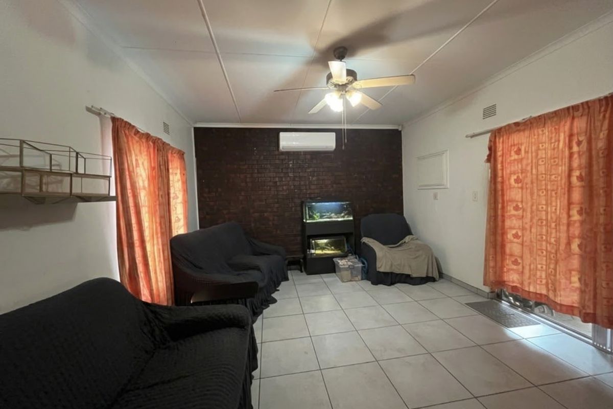 A living room featuring a dark exposed brick accent wall, tiled flooring, a ceiling fan, and a wall-mounted split-system air conditioner.