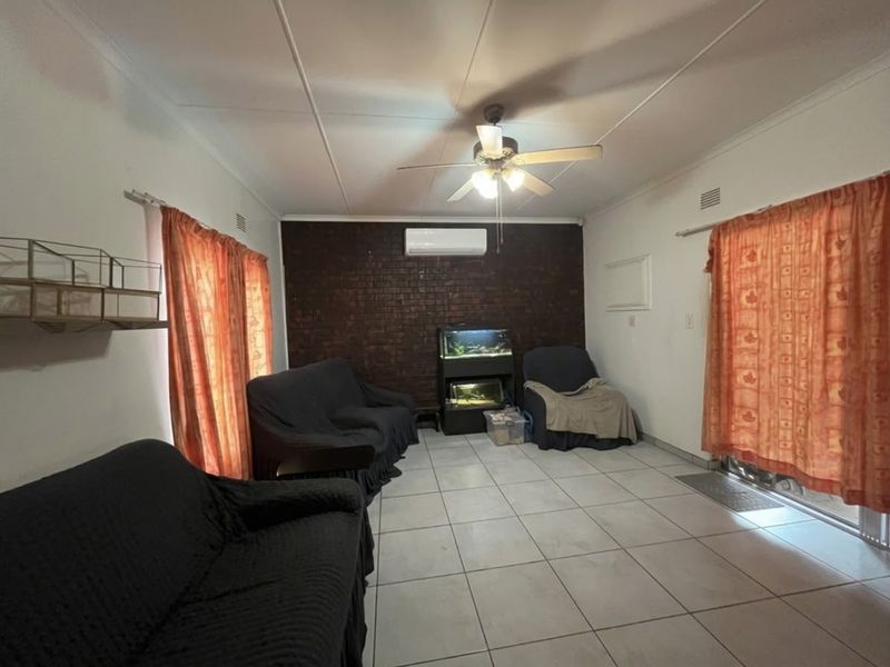 A living room featuring a dark exposed brick accent wall, tiled flooring, a ceiling fan, and a wall-mounted split-system air conditioner.