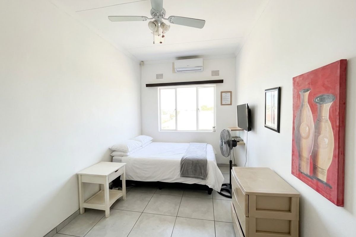 A functional bedroom featuring tiled flooring, a ceiling fan, and a wall-mounted split-system air conditioner.